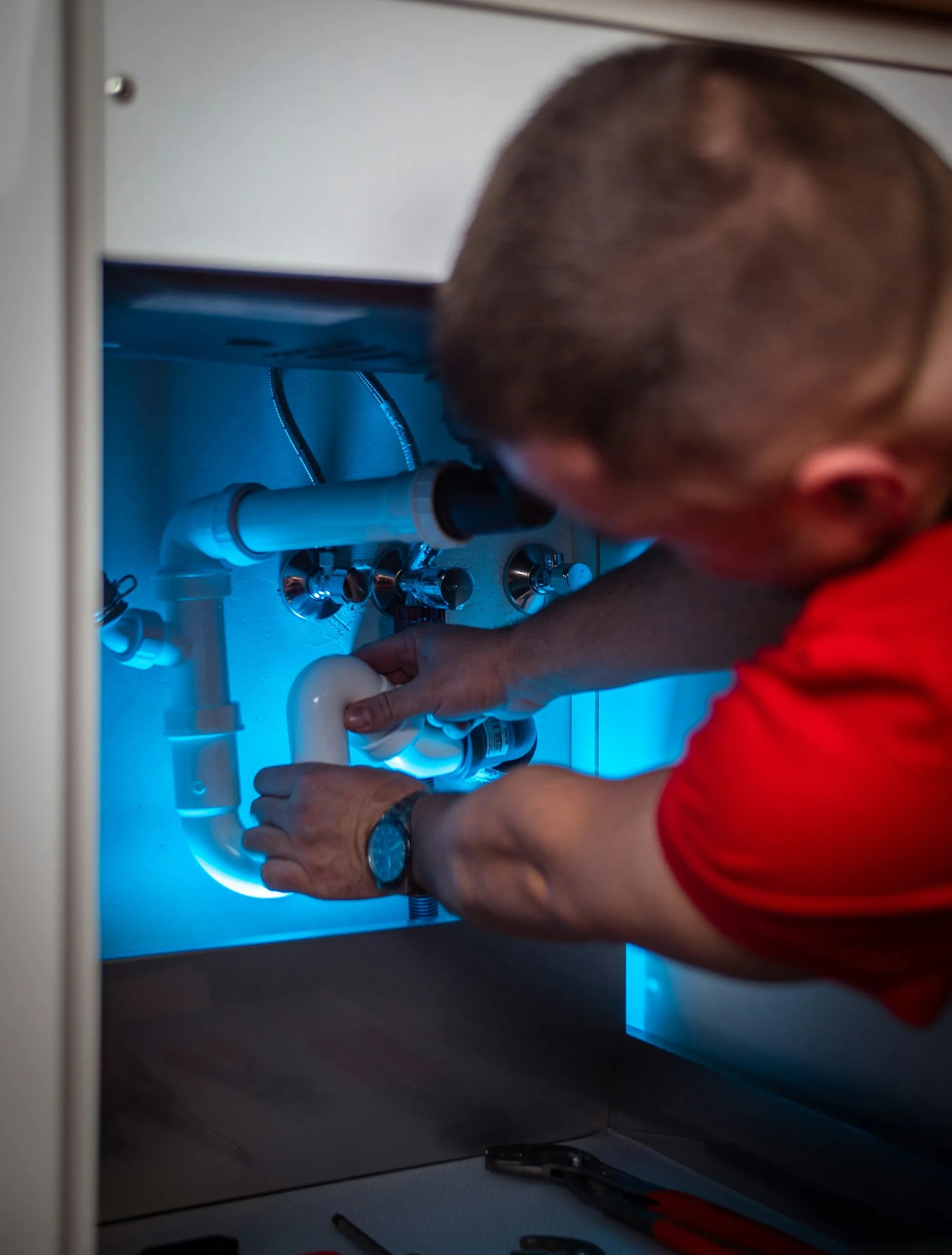 A man working on a pipe inside a cabinet