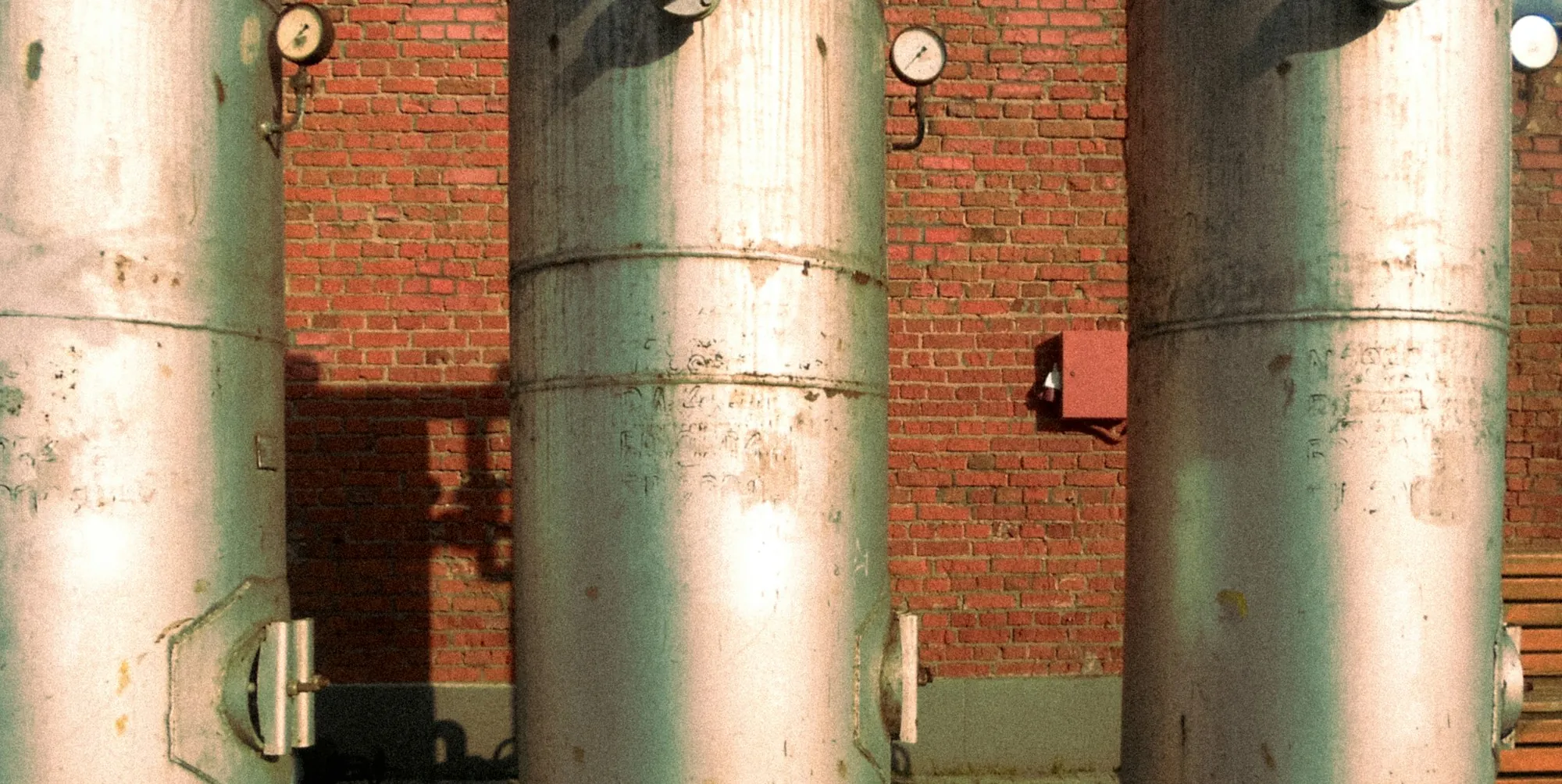 Three tall treatment tanks with pressure gauges against a brick wall